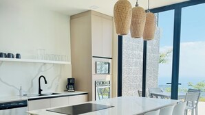 Una cocina moderna con una isla central, taburetes blancos de bar y un amplio ventanal con vistas al exterior.