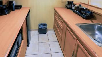 A compact kitchen with wooden cabinets, a sink, and a trash bin.