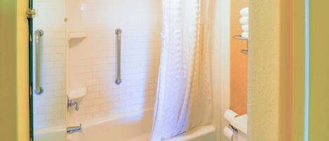 Une salle de bain avec une douche à parois de verre, des murs recouverts de carreaux blancs, une baignoire blanche et des toilettes blanches.