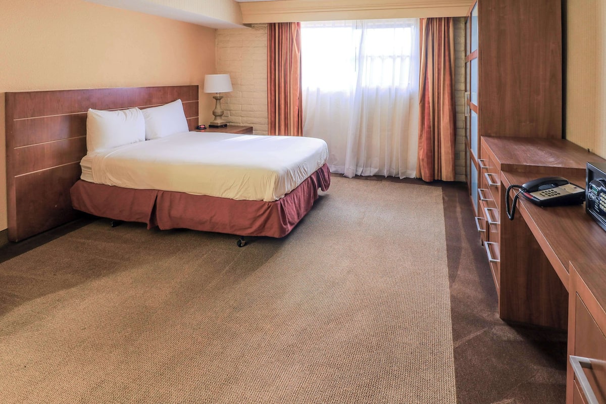 Ein Hotelzimmer mit einem großen Bett, einem Schreibtisch mit Telefon und einem Vorhangfenster.