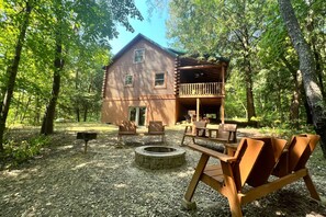 A rustic cabin with a deck, surrounded by trees.