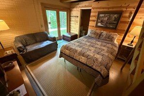 A cozy room with a bed, a sofa, and a small table. There is a window with a view of greenery outside.