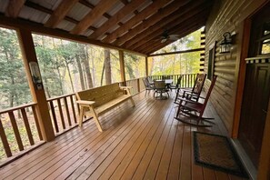 A wooden deck with a bench and chairs, overlooking a forested area.