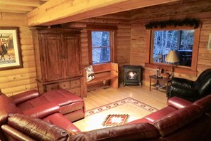 A cozy log cabin interior with a fireplace, leather sofas, and a rug.
