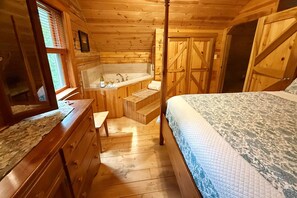 A wooden cabin bedroom with a four-poster bed, a wooden dresser, a vanity with a mirror, and a wooden door.