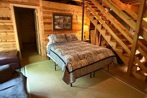 Ein Schlafzimmer in einer Holzhütte mit einem Bett, einem Nachttisch, einer Lampe und einer Treppe.