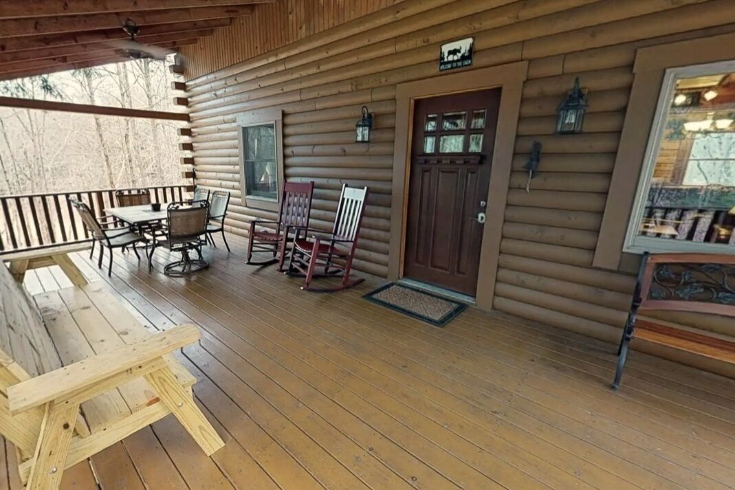 A wooden cabin with a porch, a dining table with chairs, and a rocking chair.