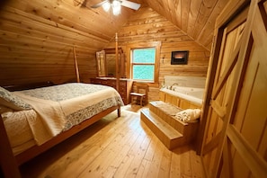 Ein gemütliches Schlafzimmer in einer Holzhütte mit einem Bett, einem Schminktisch mit Spiegel, einem Fenster und einer Badewanne.