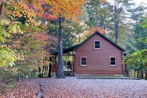 A rustic log cabin with a porch, surrounded by autumn foliage.