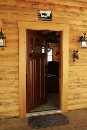 Eingang eines Holzchalets mit einer Willkommensschild, einer Glocke und einer Laterne an der Wand.