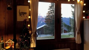 A cozy room with a wooden interior, a window with curtains, a Christmas tree, and a small table with various items. - "LES RONDINS, Guzet snow chalet, direct start to slopes and hikes, panoramic view (Ustou)