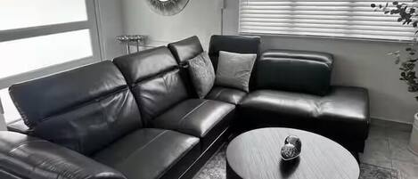 Una sala de estar moderna con un sofá seccional de cuero negro, una mesa de centro redonda y un espejo decorativo en la pared.