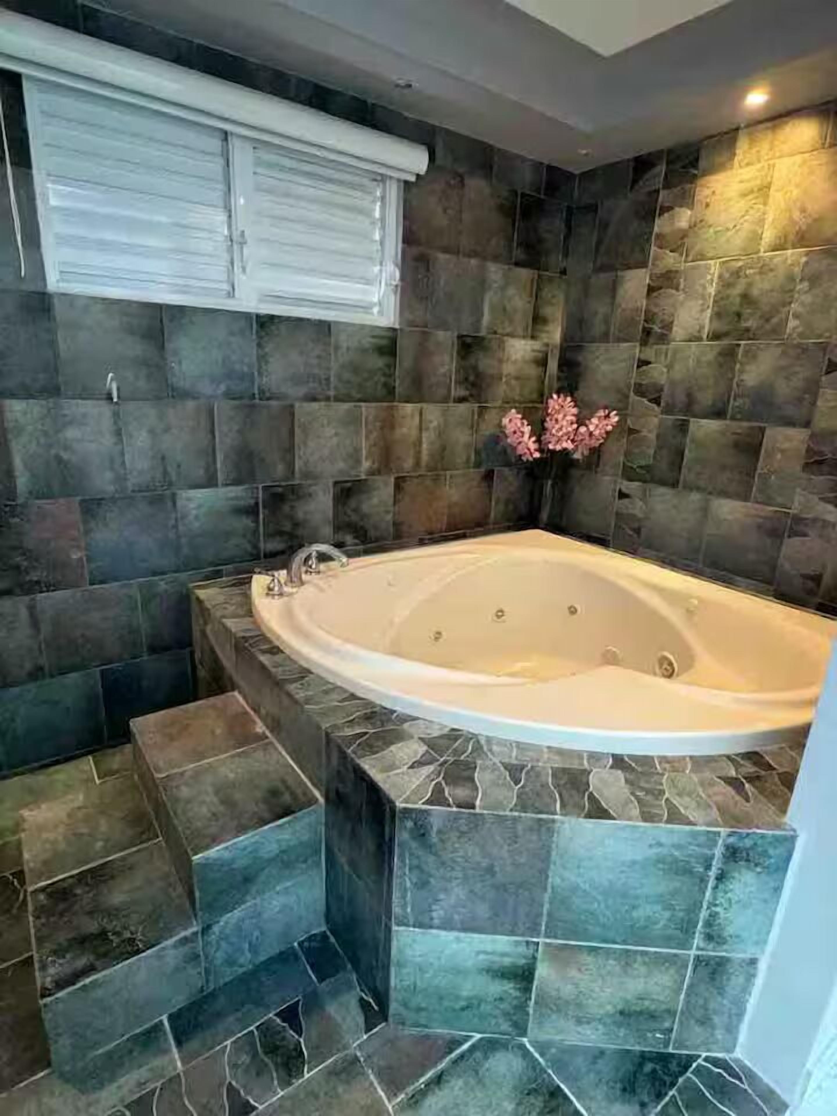 Un baño con una bañera independiente, paredes de piedra y una ventana con persianas.