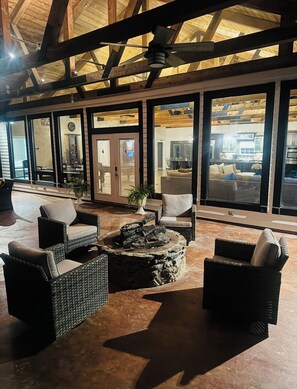 Un espacio interior amplio con mobiliario de mimbre, un hogar de piedra y grandes ventanales que ofrecen vistas del interior.