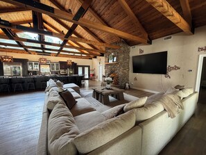 A spacious living area with a large sofa, wooden beams, a stone wall, and a flat-screen TV. - Luxury “state” of mind (Starkville)