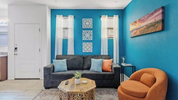 A living room with a blue wall, a grey sofa, a wooden coffee table, and an orange armchair. - Private Entry Guest Suite by AZ Athletic Grounds - 1 BD + 1 BA - Sleeps 4 (Mesa)