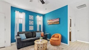 A living room with a blue wall, a black sofa, an orange chair, and a round coffee table. - Private Entry Guest Suite by AZ Athletic Grounds - 1 BD + 1 BA - Sleeps 4 (Mesa)