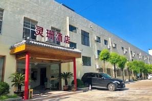 Un hotel con vestíbulo cubierto, varias ventanas y un estacionamiento con automóviles.
