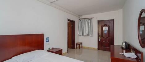 A hotel room with a bed, a desk, a chair, a mirror, and a door.