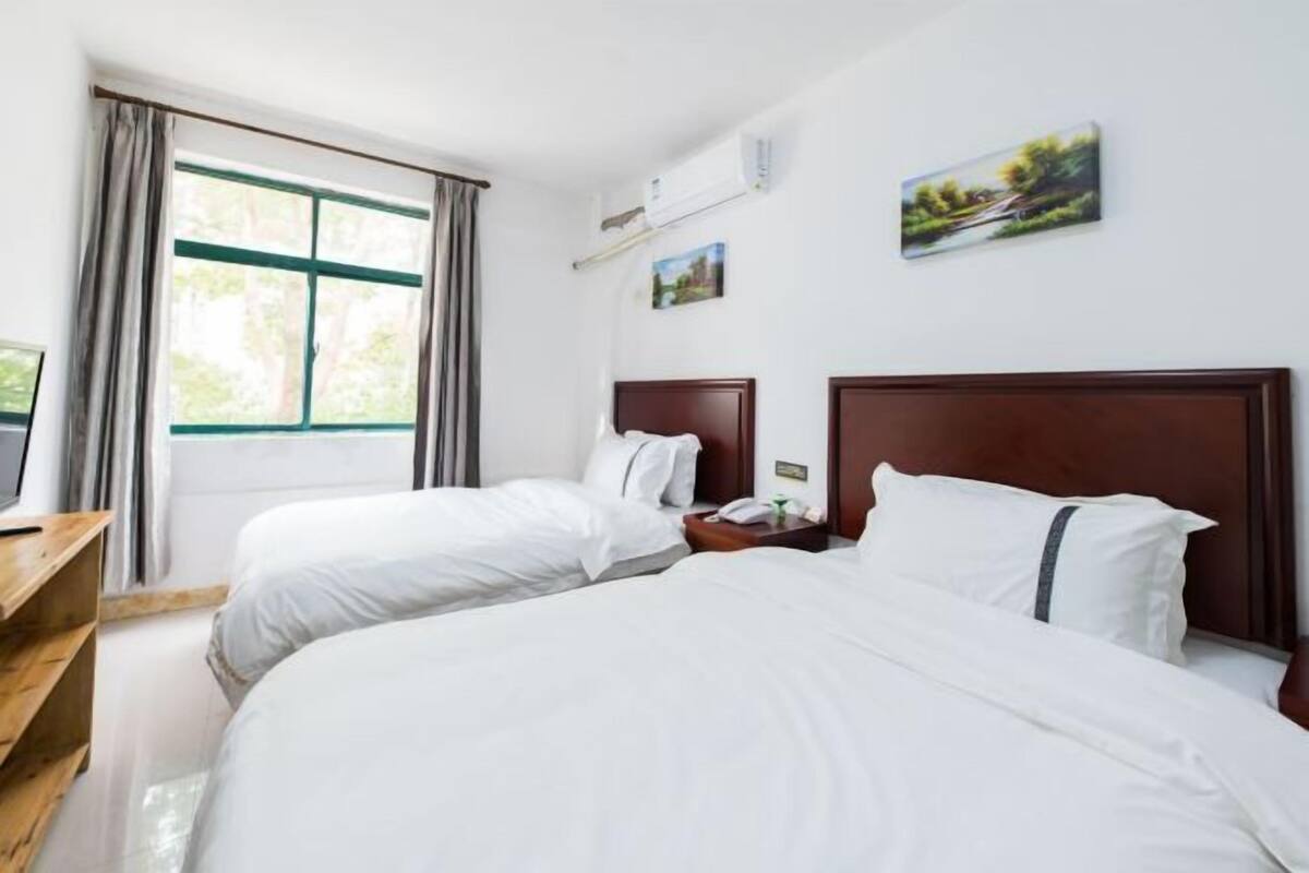 A hotel room with two beds, a wooden desk, a window with curtains, and a painting on the wall.