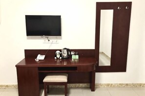 Un escritorio de madera con un televisor, un espejo, un teléfono y una mesita con una tetera y tazas.