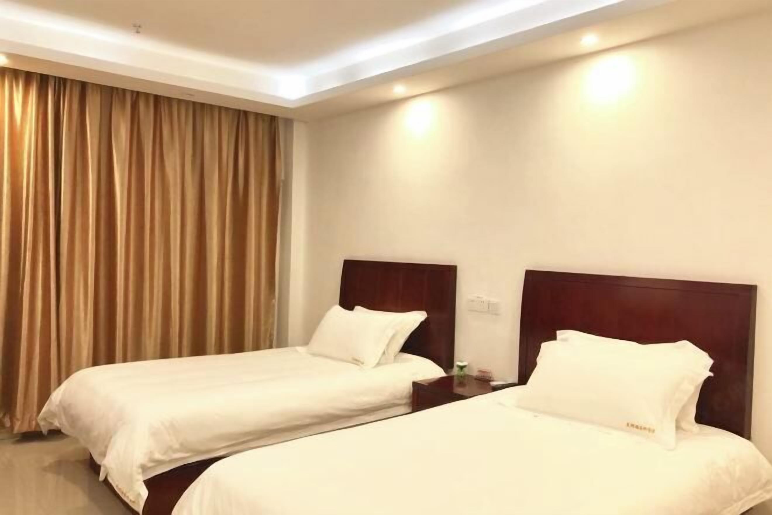 Quarto de hotel com duas camas de solteiro, cabeceira de madeira, mesa de cabeceira e uma janela grande com cortinas.