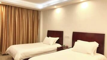 Quarto de hotel com duas camas de solteiro, cabeceira de madeira, mesa de cabeceira e uma janela grande com cortinas.