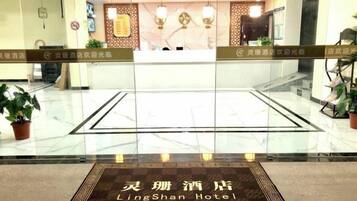 A hotel reception area with a marble floor, reception desk, and potted plants.