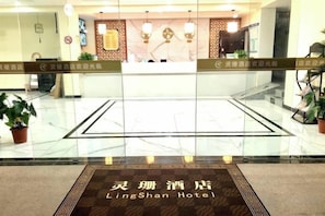A hotel reception area with a marble floor, reception desk, and potted plants.
