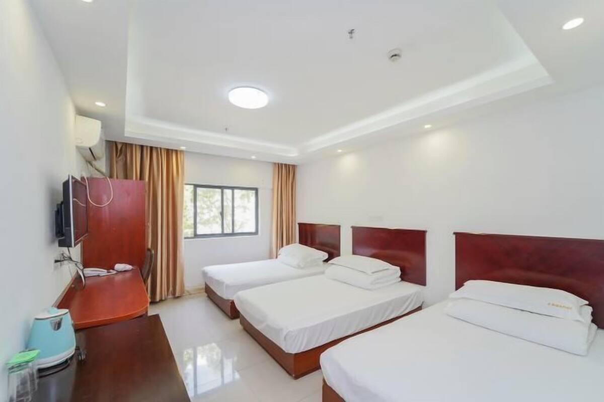 A hotel room with two beds, a desk with a chair, a television, and a window with curtains.