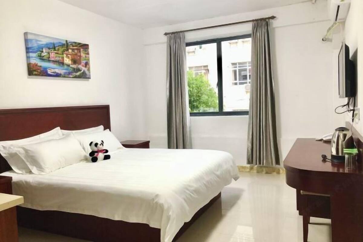 A hotel room with a bed, a desk, a TV, and a window with curtains.