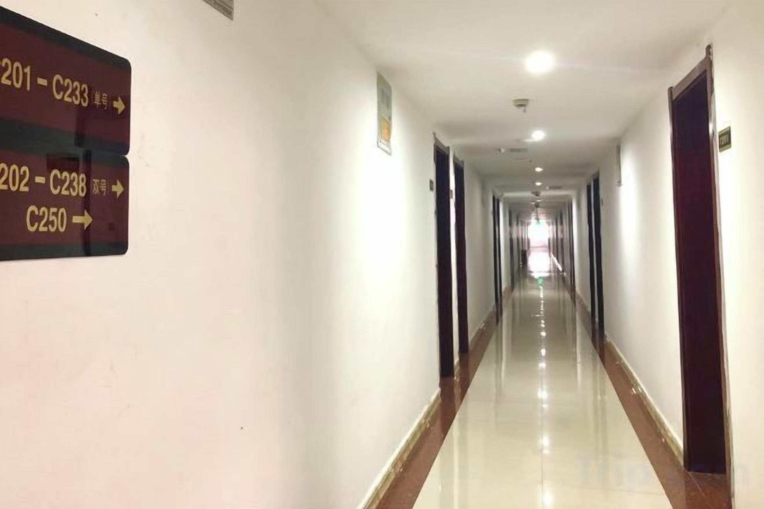 A long, straight corridor with directional signs on the left wall indicating room numbers and corresponding codes.