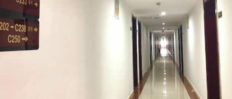 A long, straight corridor with directional signs on the left wall indicating room numbers and corresponding codes.