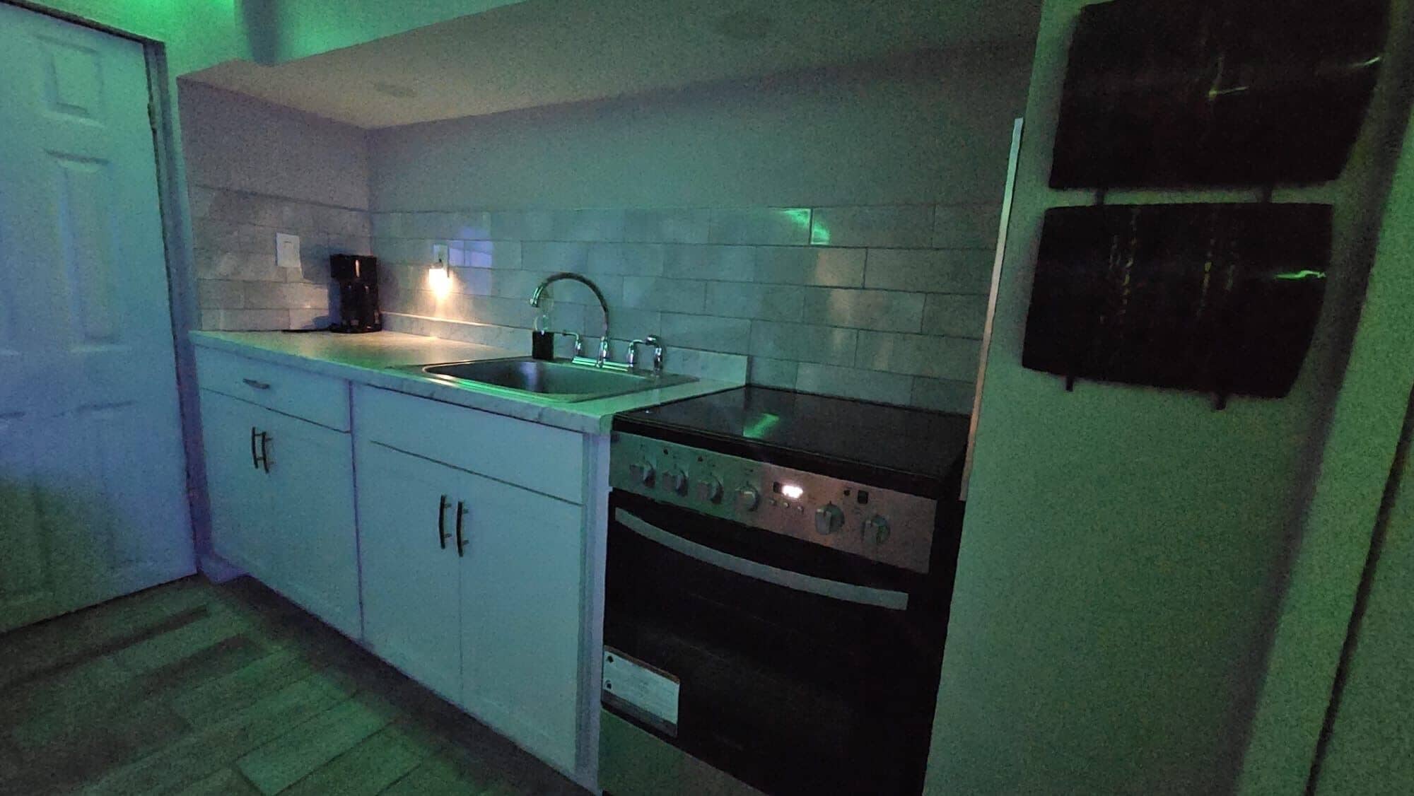 A compact kitchen with white cabinets, a stainless steel sink, a stove, and a built-in oven.