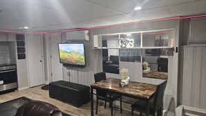 A modern living room with a flat-screen TV, a dining area with a table and chairs, and a kitchen area with a stove and microwave. - Lofty Cozy Suite near Nassau Coliseum and Hofstra University (Hempstead)