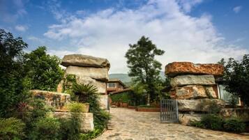 A stone pathway leading to a building with a metal gate, surrounded by greenery and large rock formations.