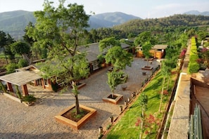 Une cour agrémentée de pavillons, d’arbres et offrant une vue sur des montagnes lointaines.