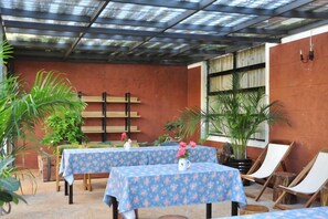 Un patio al aire libre con mesas y sillas, rodeado de plantas en macetas.