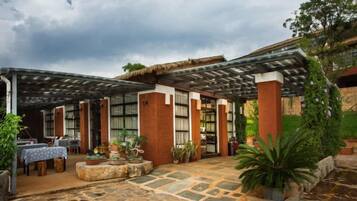 A covered outdoor area with stone flooring, potted plants, and a thatched roof structure.