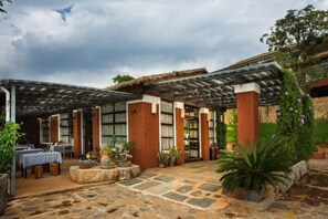 Un espace extérieur abrité, doté d’un sol en pierre, de plantes en pot et d’une structure de toit en chaume.