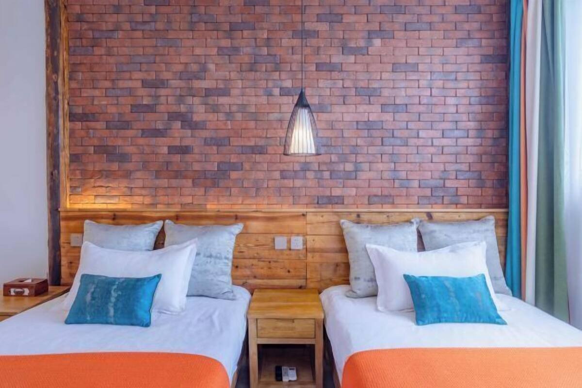 Een hotelkamer met twee bedden, een bakstenen muur, een houten hoofdeinde en een hangende lamp.