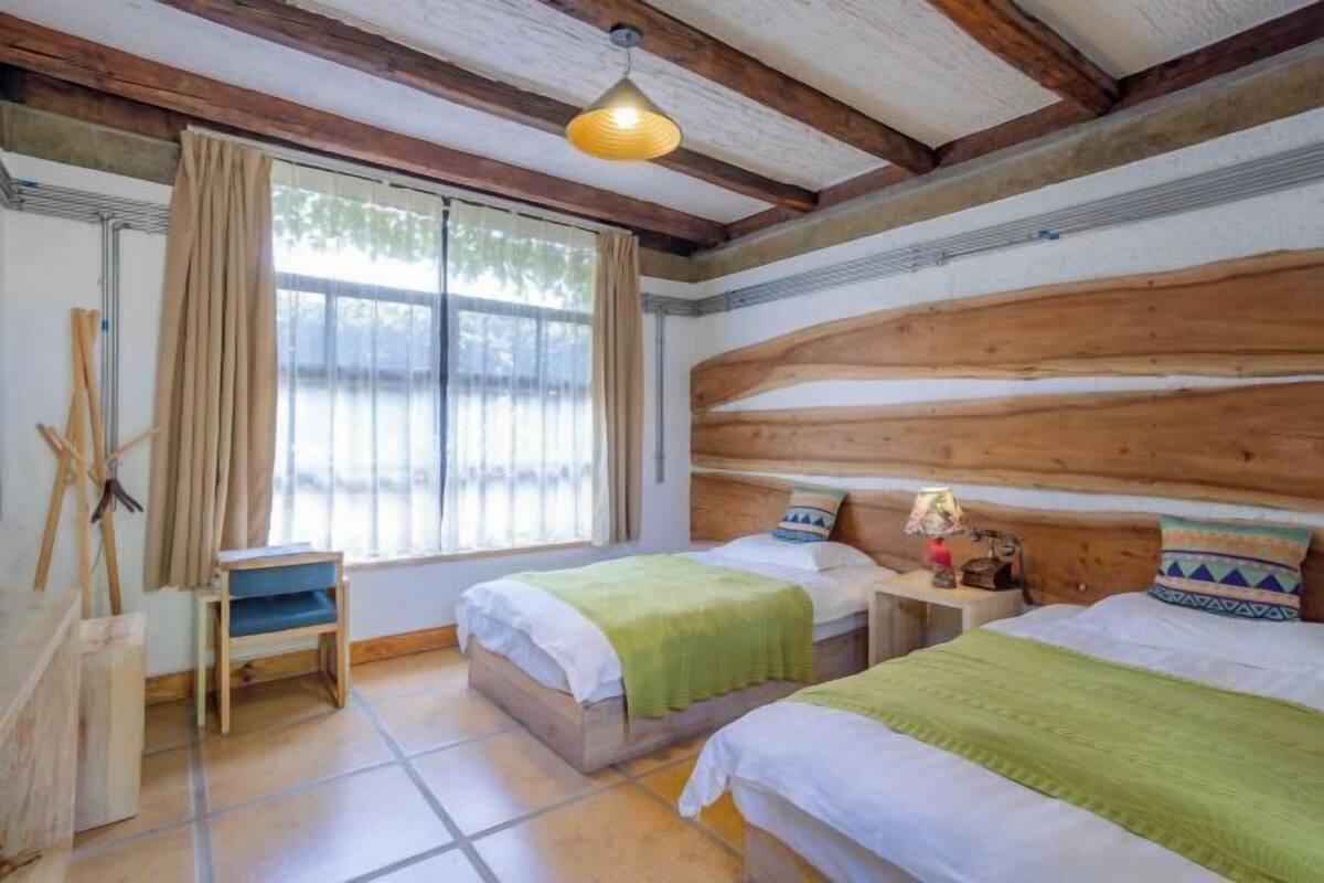 Een kamer met twee bedden, een raam met gordijnen, een houten plafond en een kleine tafel met een lamp.
