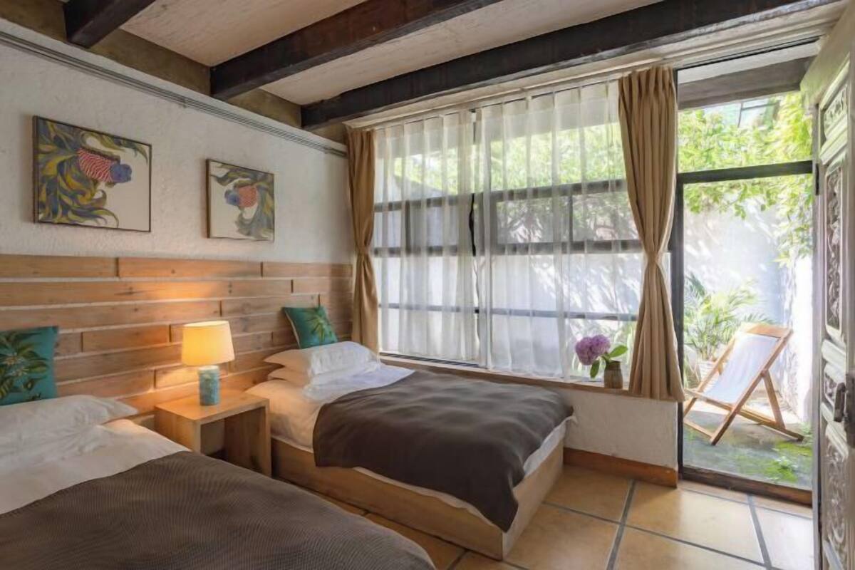 Een kamer met twee bedden, een raam met dunne gordijnen, een houten hoofdbord en kunst aan de muur.
