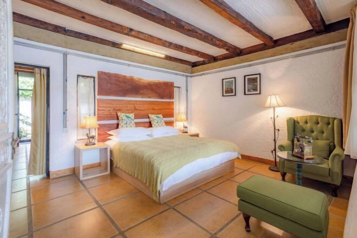 Een slaapkamer met een groot bed, een groene fauteuil, een tafeltje en een lamp.