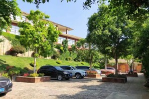 Un estacionamiento con autos y árboles, un edificio con techo inclinado, y un cielo despejado.