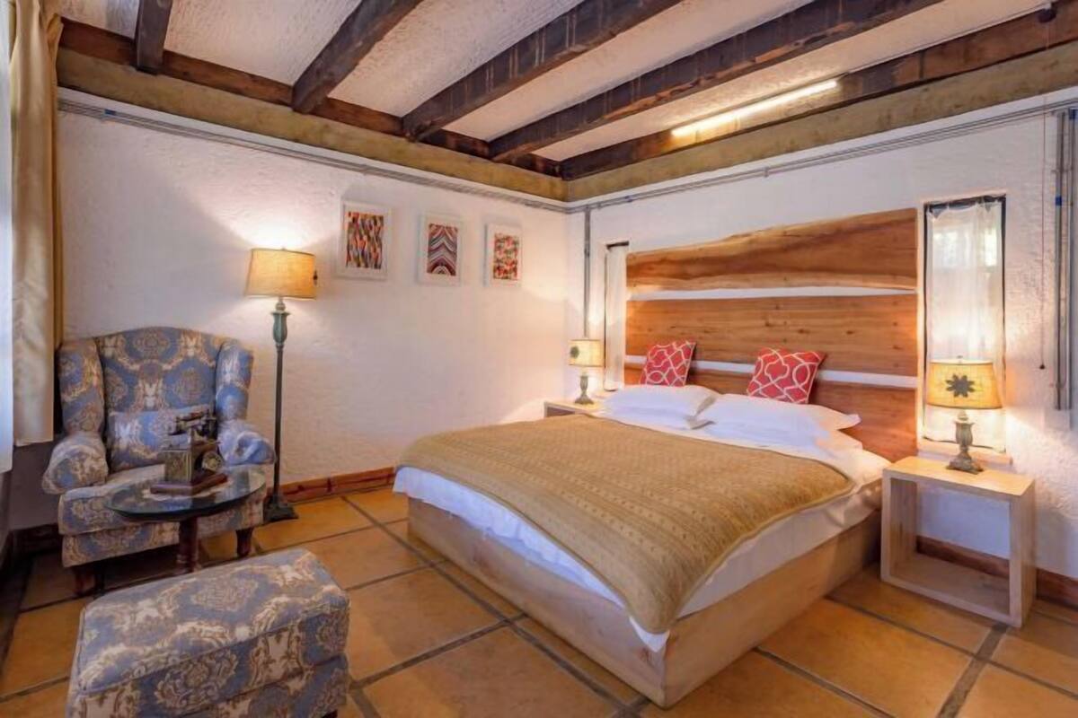 Een slaapkamer met een groot bed, een stoel, een klein tafeltje en een houten hoofdbord.