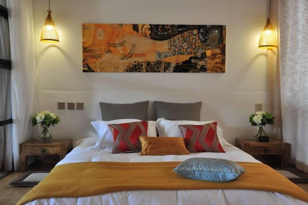 Een hotelkamer met een groot bed, twee nachtkastjes, een aan de muur hangend schilderij en twee wandlampen.
