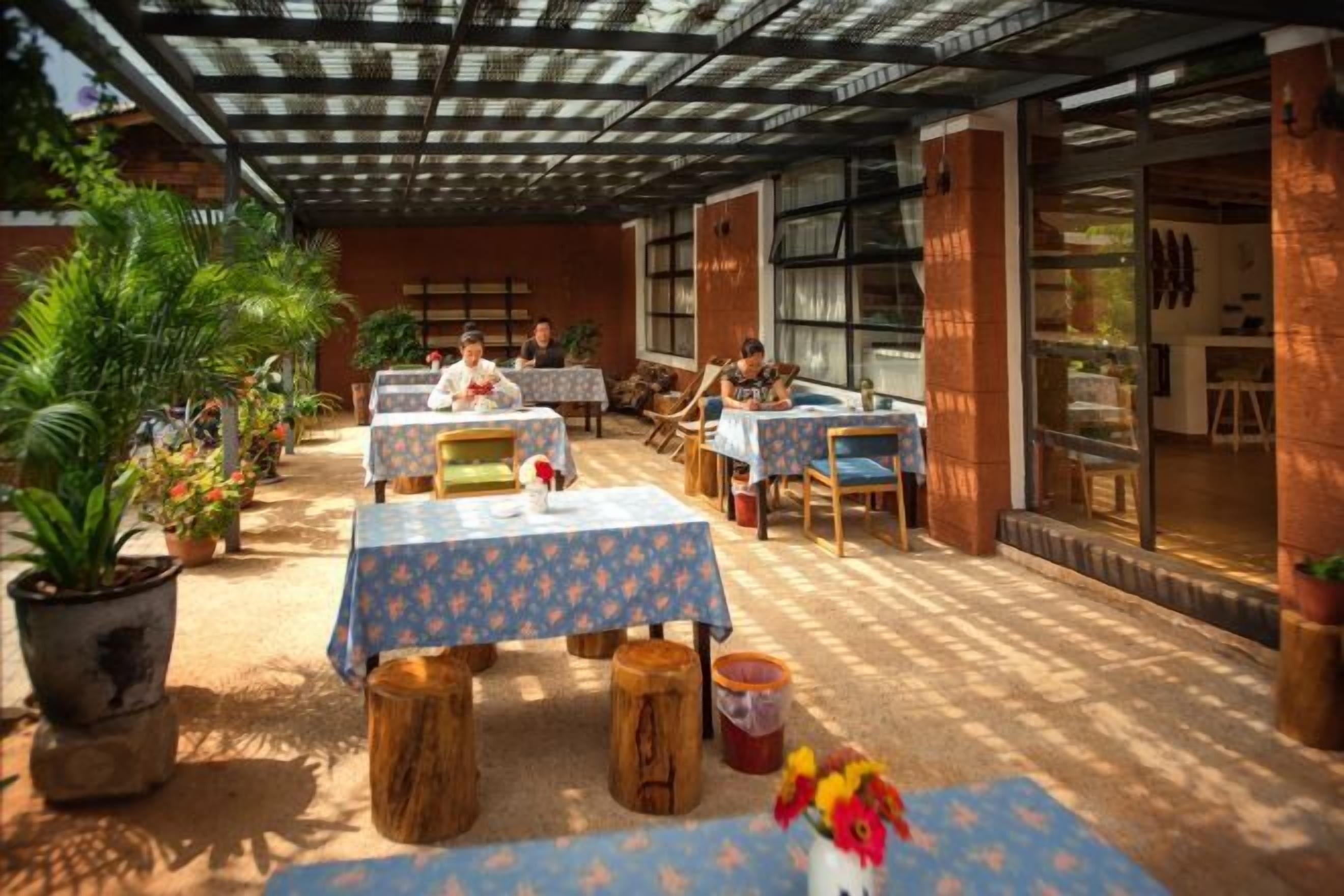 An outdoor patio with tables and chairs, potted plants, and a covered area with a view of the interior.