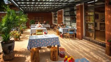 An outdoor patio with tables and chairs, potted plants, and a covered area with a view of the interior.