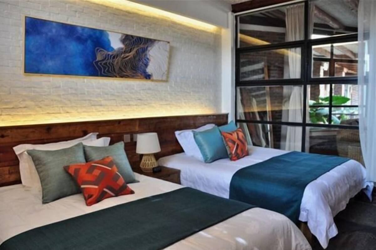 Een hotelkamer met twee bedden, een groot raam, een schilderij aan de muur en een houten hoofdeinde.